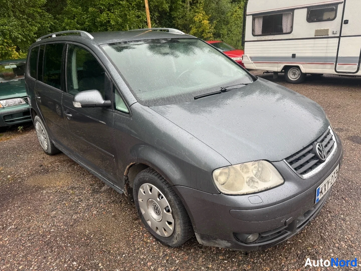 Etuviisto, nokka oikealle: Tummanharmaa tila-auto kuvattu kolmasosakulmasta keulaa oikealle kääntyneenä, katolle asennetut kaiteet ja Volkswagen-merkki jäähdyttimen suojassa. Recol