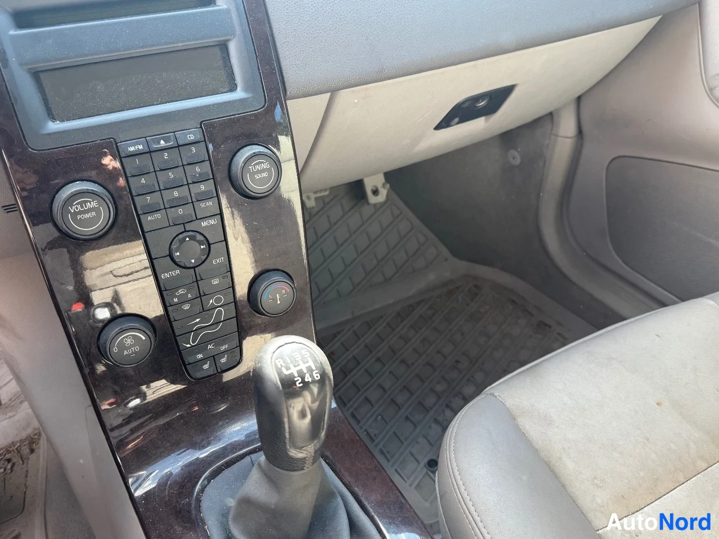 Yksityiskohta: Center console close-up showing manual gear lever with white 5-speed pattern, radio/media panel, climate control buttons, and glovebox area.