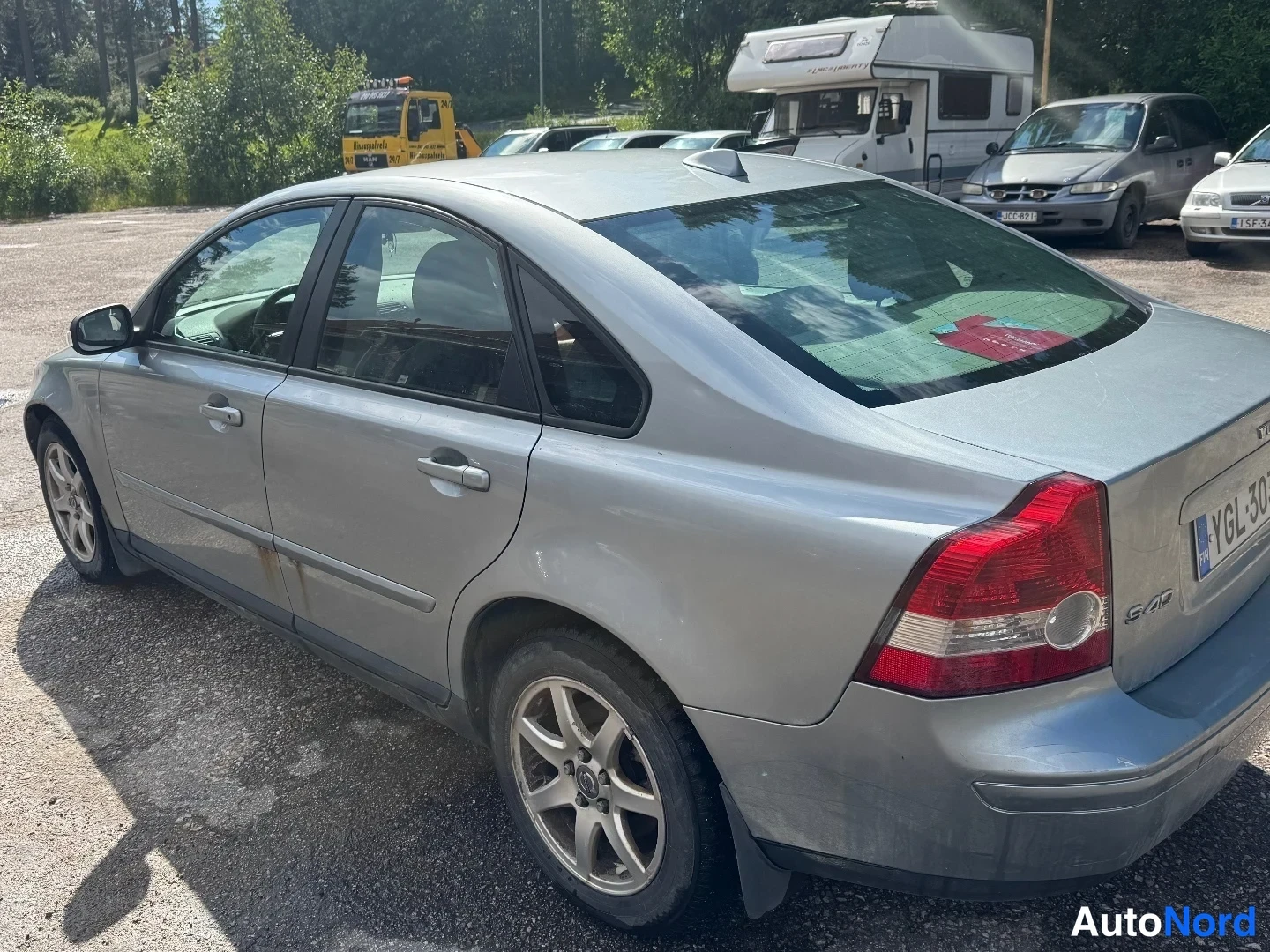 Takaviisto: Silver four-door Volvo S40 sedan seen from the rear left side in a gravel parking lot, showing the trunk with 'S40' badge and alloy wheels.