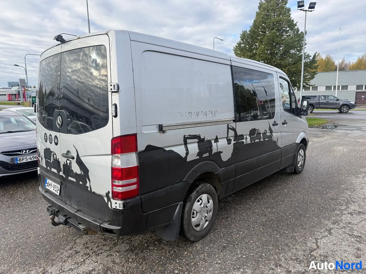 Takaviisto: Hopeanharmaa pakettiauto taka­kolmannes­kulmassa vasemmalta, takapöttelö ja vasen sivu näkyvissä.