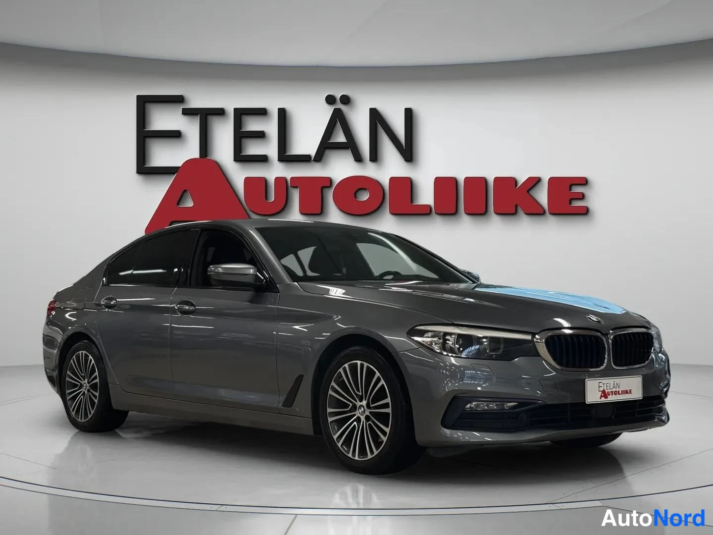 Etuviisto, nokka oikealle: BMW 520 -sedan etuviisto vasemmalta, tummanharmaa kori ja kevytmetallivanteet studioympäristössä.