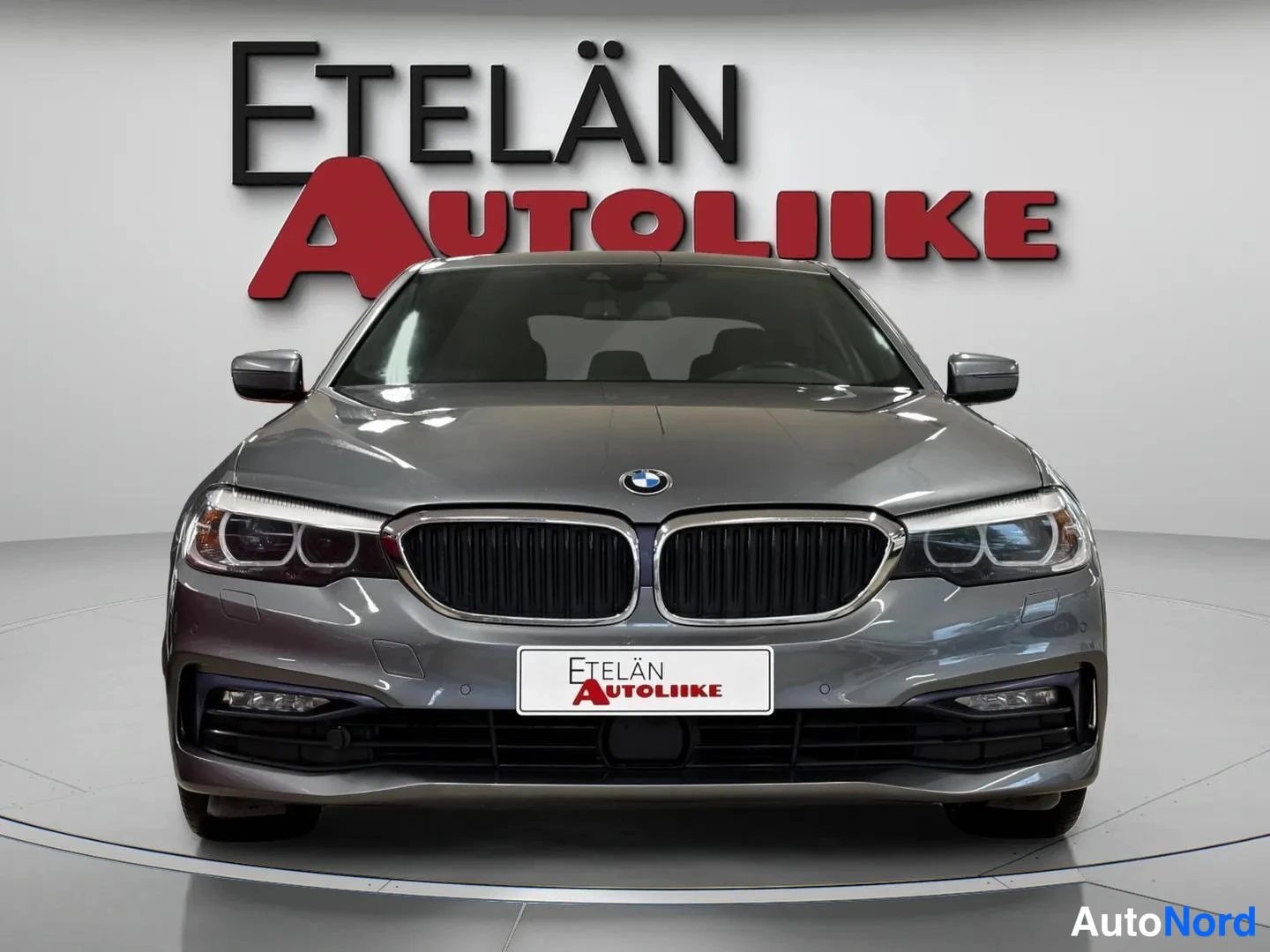 Edestä: BMW 520 -sedan etunäkymä suoraan edestä, tummanharmaa kori, BMW-merkki konepellissä ja Etelän Autoliike -kyltti etupuskurissa.