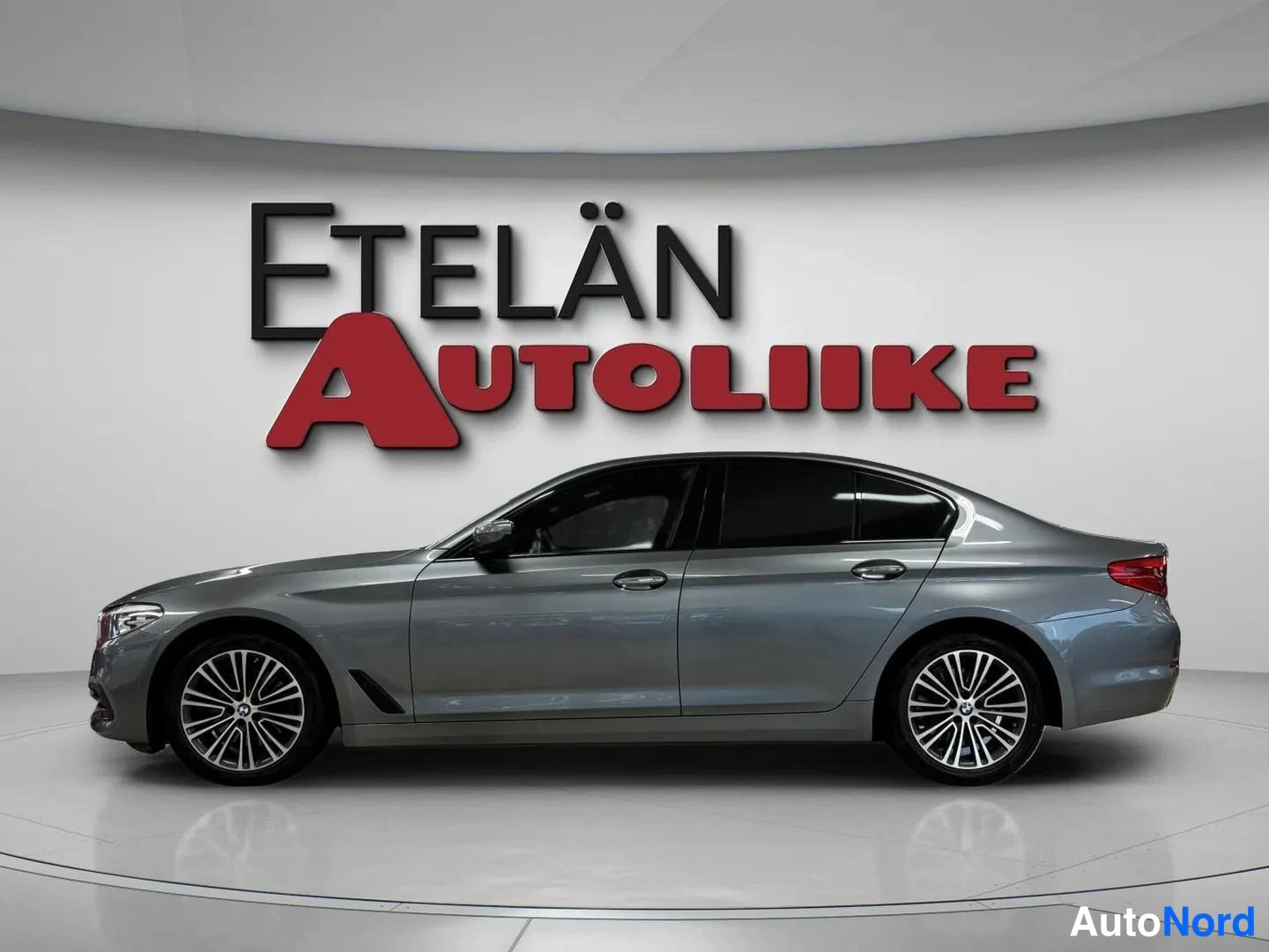 Sivulta: BMW 520 -sedan sivunäkymä vasemmalta, tummanharmaa kori, kevytmetallivanteet ja tummat ikkunat.