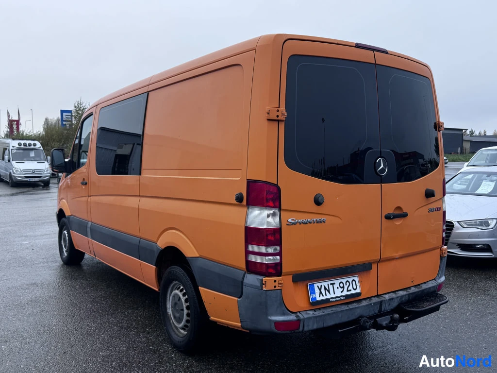 Takaviisto: Oranssi Mercedes-Benz Sprinter takaviistolta vasemmalta kuvattuna; kyljen liukunäkymä, rekisterikilpi ja vetokoukku näkyvät.