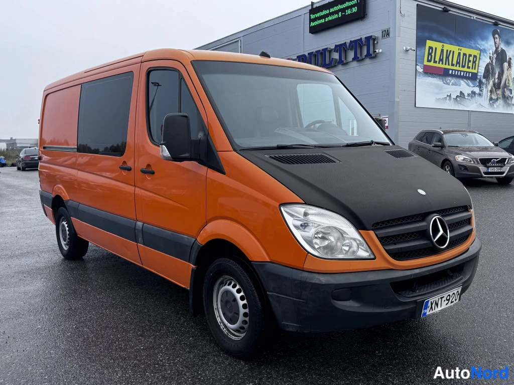 Etuviisto, nokka oikealle: Oranssi Mercedes-Benz Sprinter kolmivartalo edessä vasemmalla, musta huppu ja rekisteri.