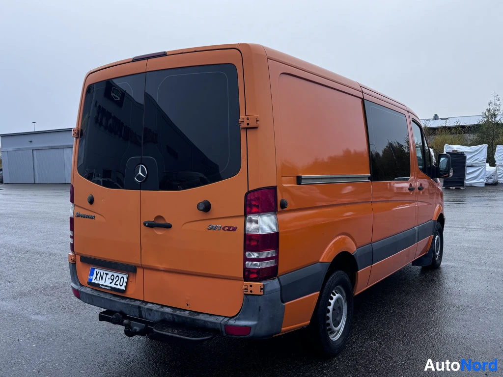 Takaviisto: Oranssi Mercedes-Benz Sprinter -pakettiauto takaviistolta kuvattuna; rekisterikilpi, kolme takavaloa ja vetokoukku näkyvät.