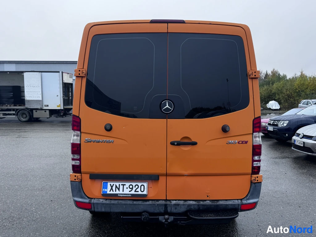 Takaa: Oranssi Mercedes-Benz Sprinter suoraan takaapäin kuvattuna; Sprinter- ja 313 CDI -tekstit, rekisterikilpi ja vetokoukku näkyvät.