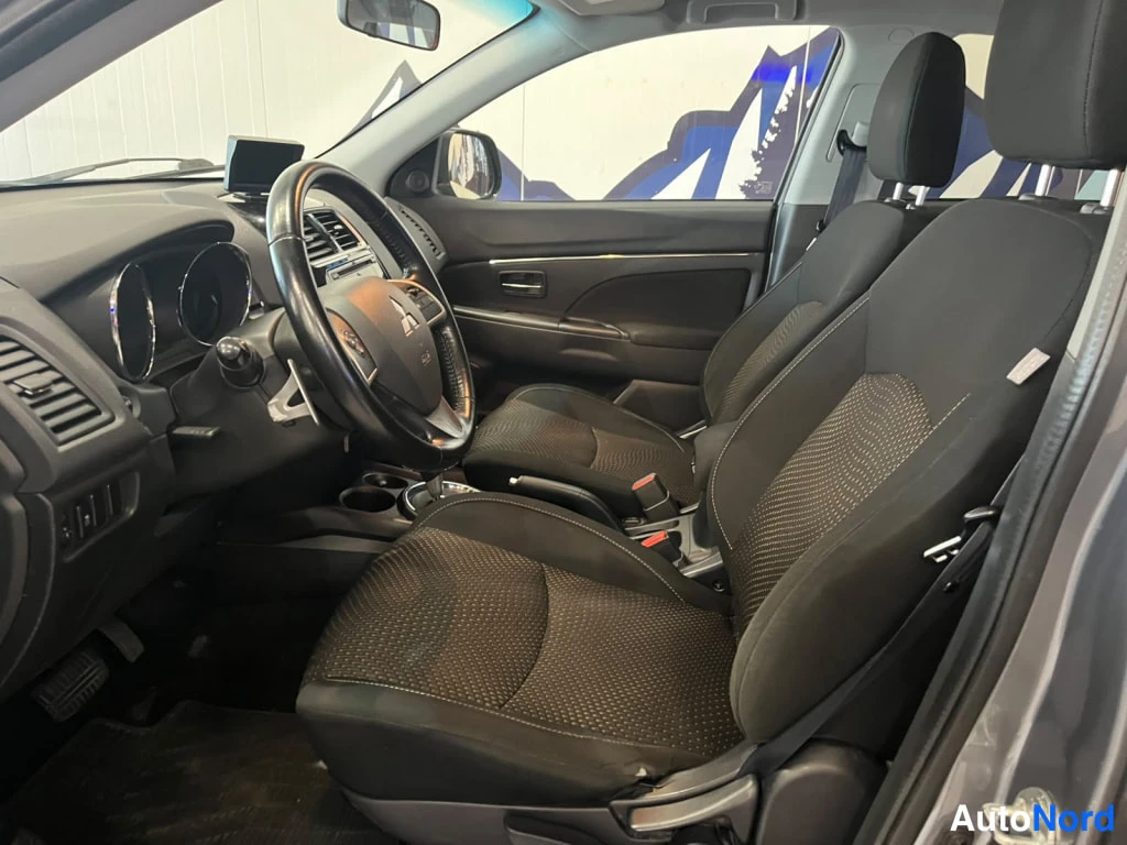 Sivulta: Auton etupenkit ja kojelauta tummalla kankaalla verhoiltuna, ratissa Mitsubishi-merkki.