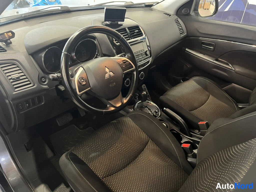 Sivulta: Auton ohjaamosta näkyy Mitsubishi-merkillinen ratikka, kojelauta ja tummat etupenkit.