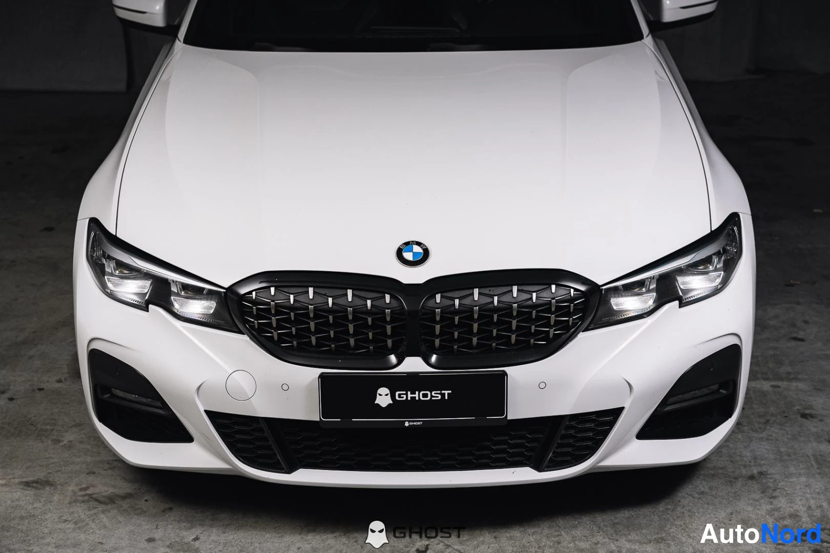 Edestä: Lähikuva valkoisen BMW:n etuosasta, tumma säleikkö ja ajovalot suoraan edestä.