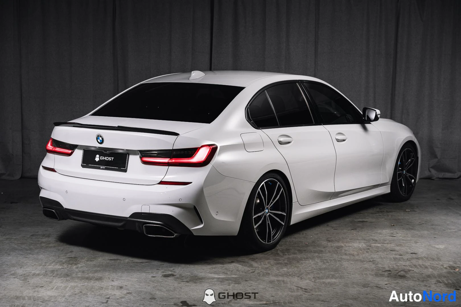 Takaviisto: Valkoinen BMW-sedan takaa oikealta kuvattuna, tummat kevytmetallivanteet, kaksoispakoputket.