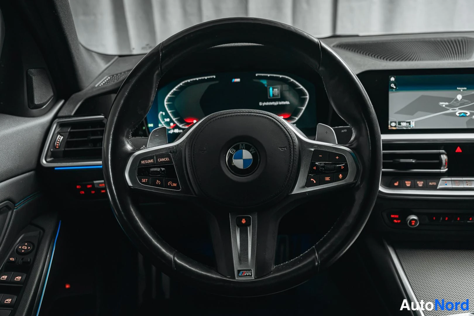 Muu: BMW-ohjauspyörä lähikuvassa, taustalla digitaalinen mittaristo ja osa keskinäytöstä.