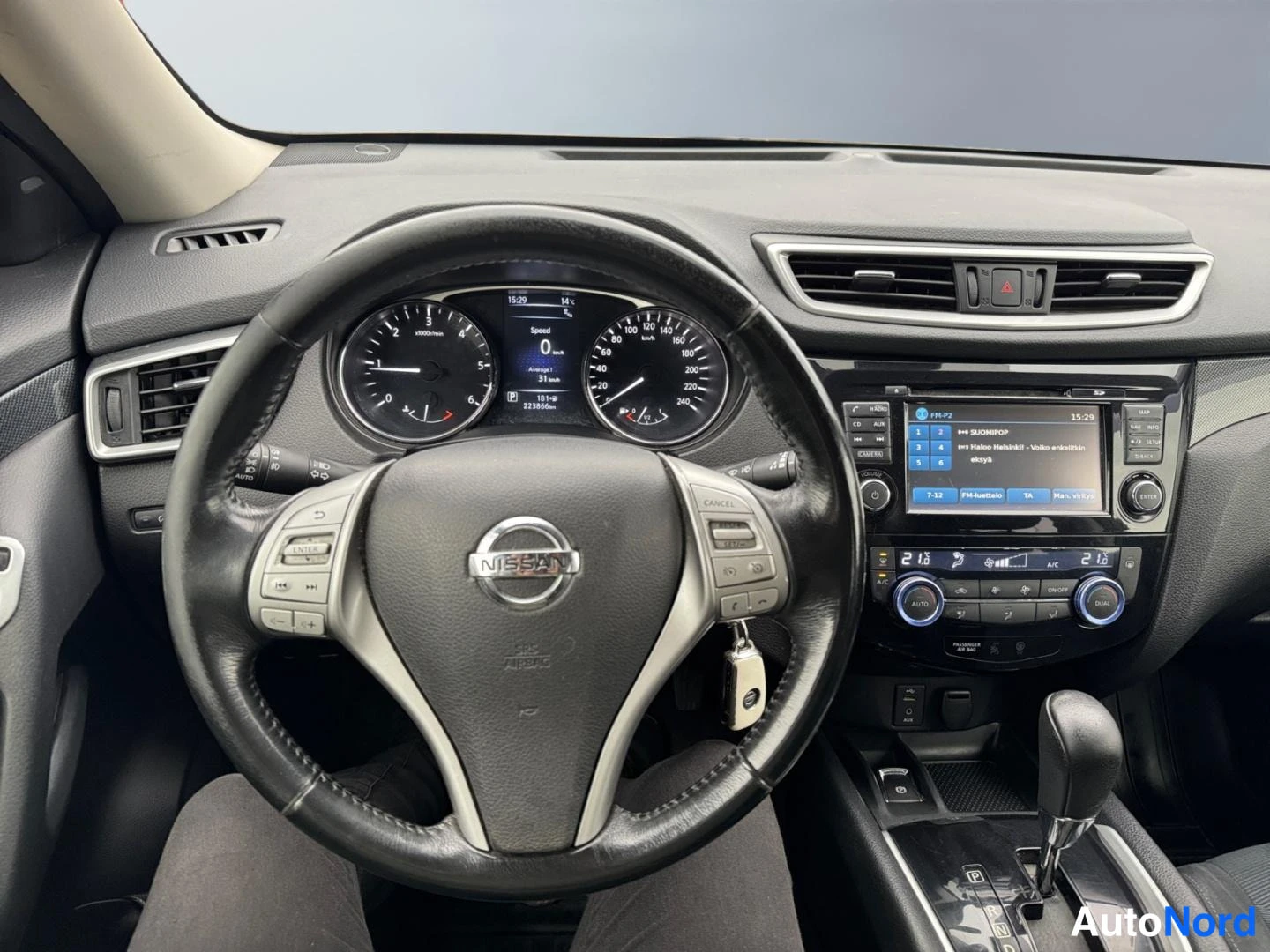 Edestä: Ohjauspöytä: Nissan-ohjauspyörä, mittaristo, kosketusnäyttö ja kaksialueinen automaatti-ilmastointi; näyttö näyttää musiikkisoittolistan.