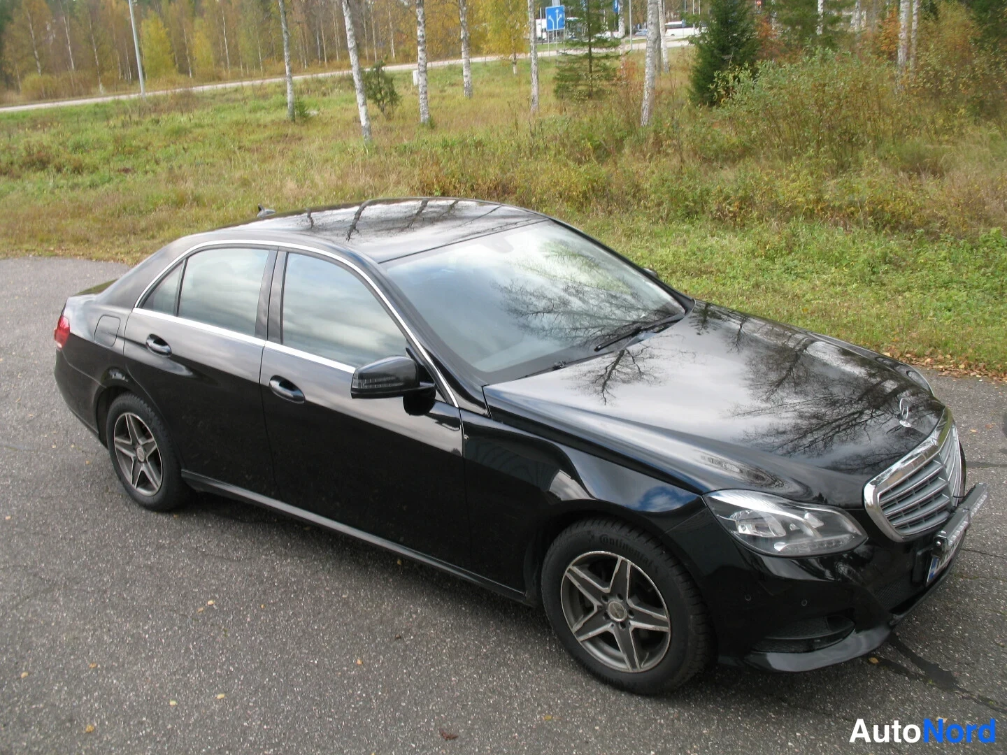 Etuviisto, nokka oikealle: Mustan sedanin keula ja oikea kylki kulmasta; koko auto näkyy mustana kevytmetallivanteilla.