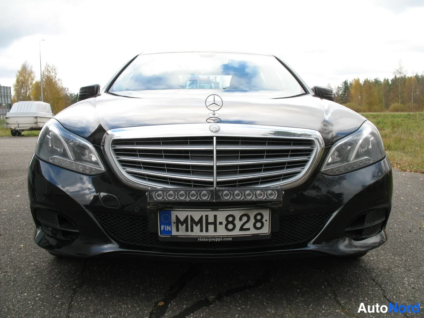Edestä: Mustan sedanin etupää suoraan edestä, Mercedes-tähti konepellillä, rekisterikilpi.