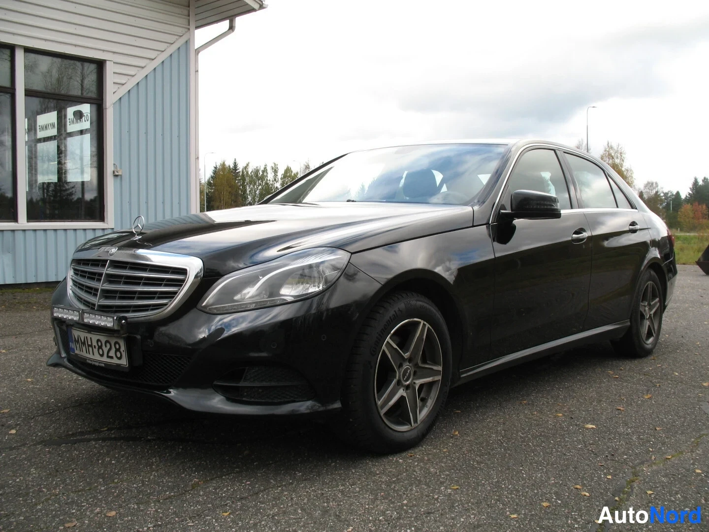 Etuviisto, nokka vasemmalle: Musta Mercedes-Benz-sedan etu kolmasosakulma, kylki ja etupusta näkyvät, rekisteritunnus.