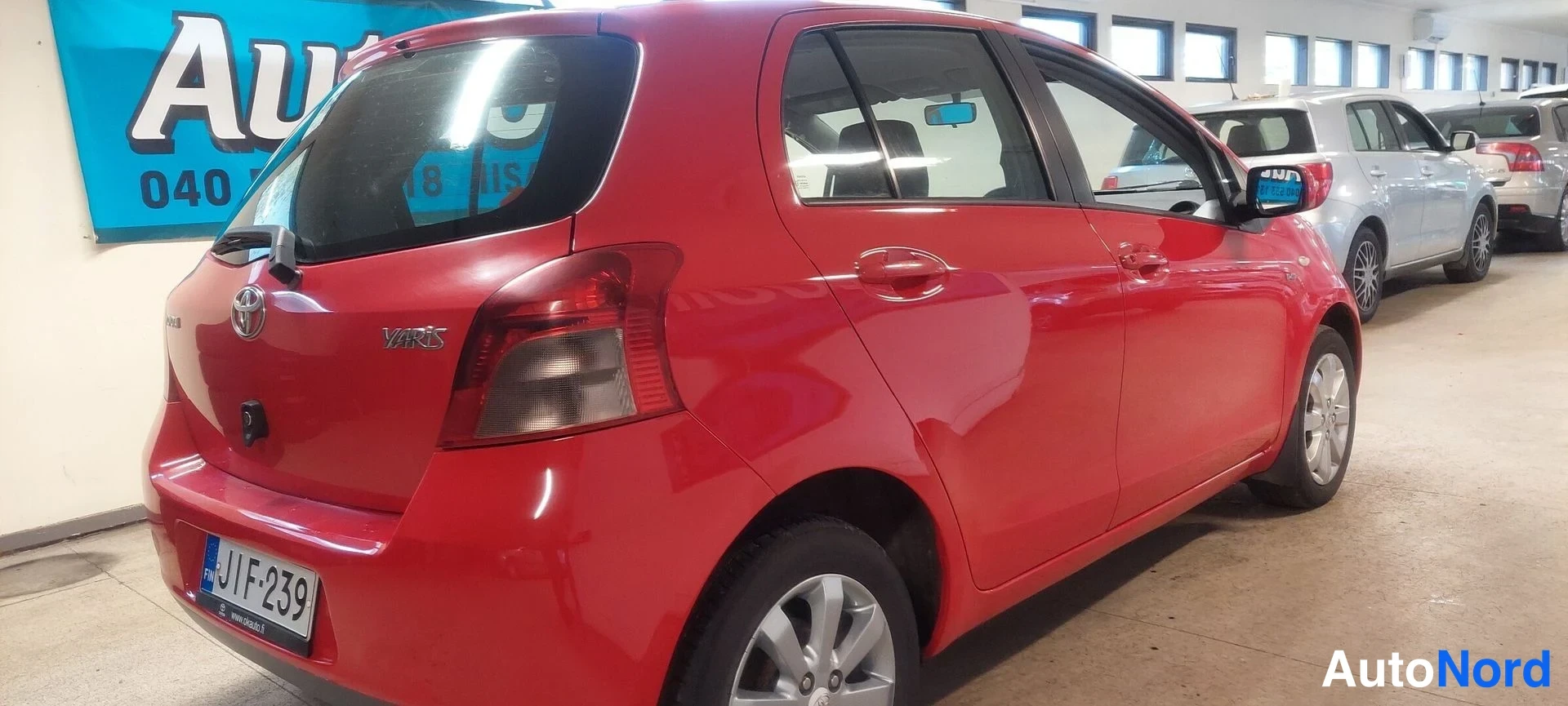 Takaviisto: Punainen Toyota Yaris -henkilöauto takaviistosta, rekisterikilpi näkyvissä.