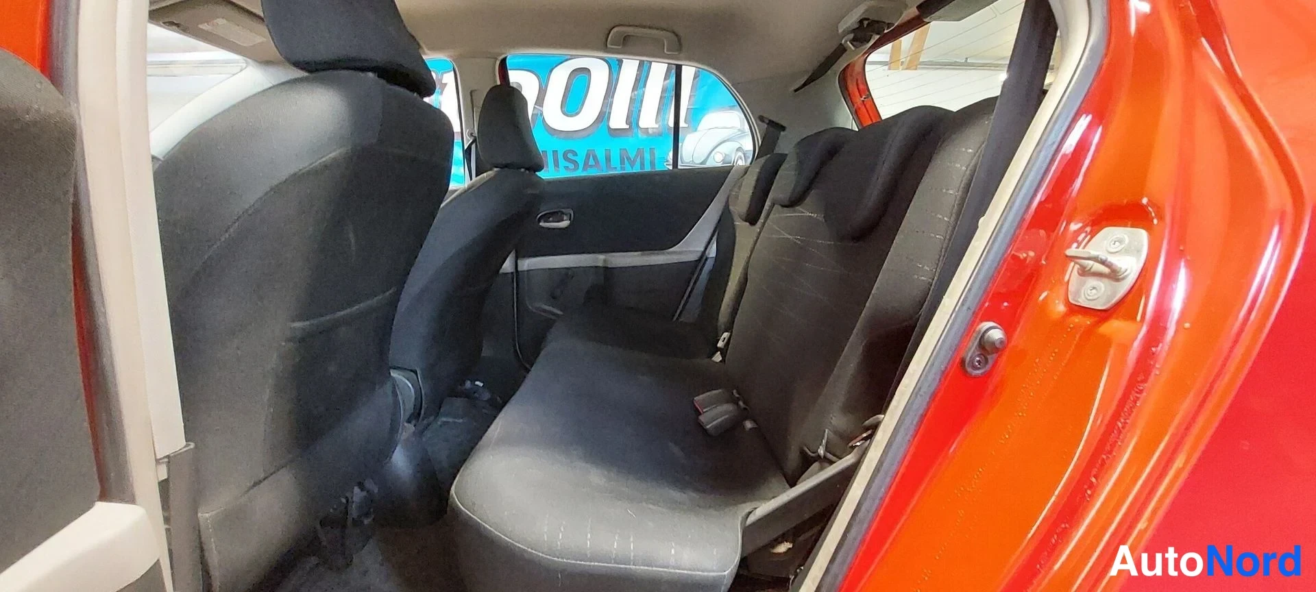 Muu: Takapenkki ja etumatkustajan istuin mustaa kangasta, takaovi auki punainen kori näkyvissä.