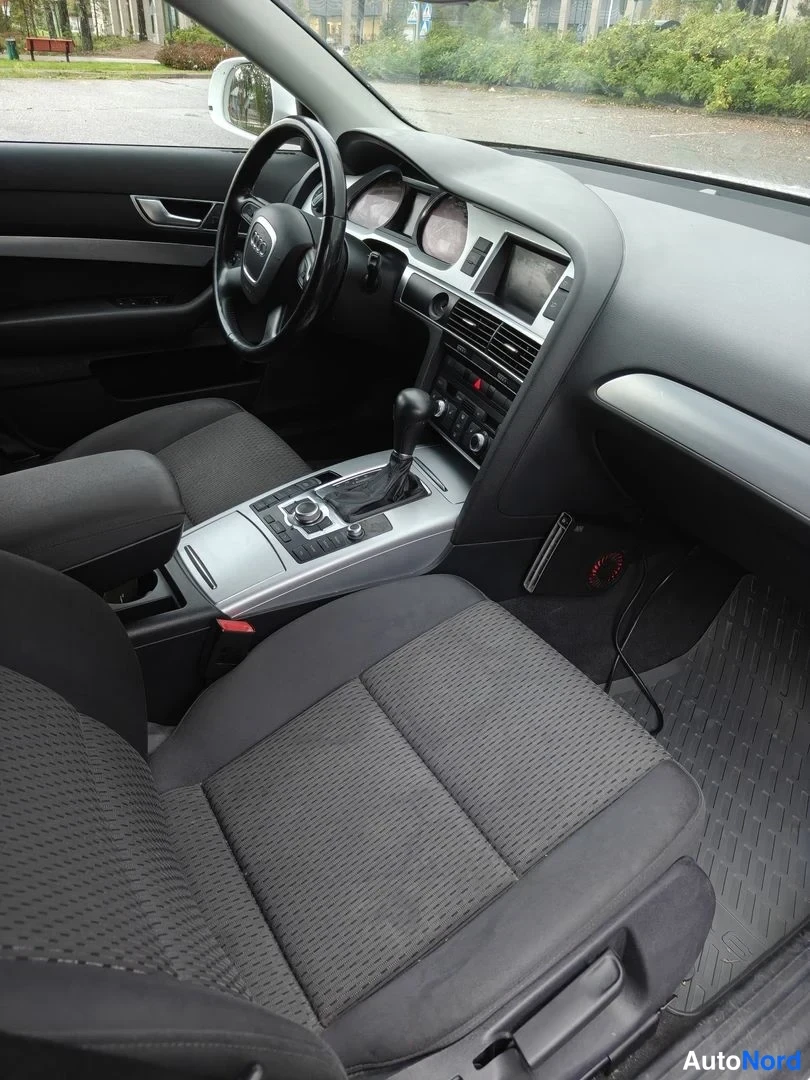 Muu: Audi A6:n sisätilat kuljettajan puolelta: tumma kangasverhoillut etuistuimet, monitoimiohjautu, MMI-keskusnappien automaattivaihteiston valitsin ja keskikonsoli