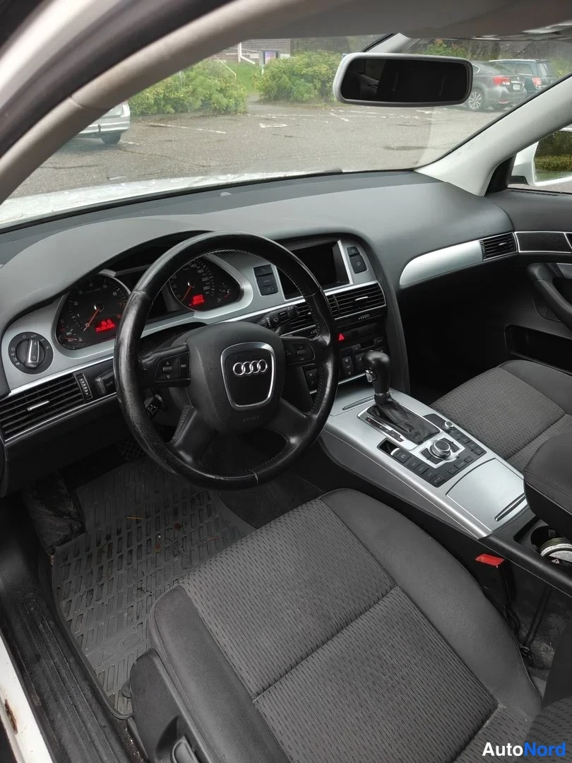 Muu: Kuljettajan näkymä Audi A6:n ohjaamoon: Audi-merkillinen ohjautu, mittaristo, keskikonsolin automaattivaihteiston valitsin ja tummat kangasistuimet.