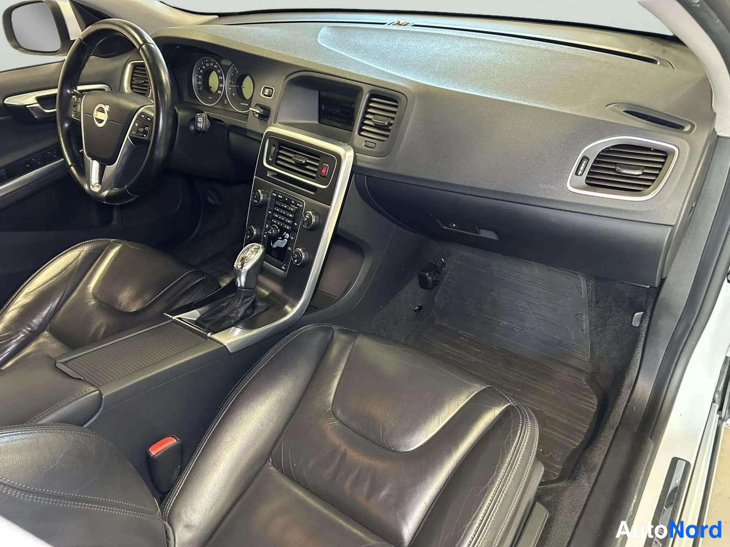 Muu: Volvo V60:n kojelauta ja keskikonsoli matkustajan puolelta kuvattuna; automaattivaihteen valitsin, mustat nahkaistuimet ja kumimatot.