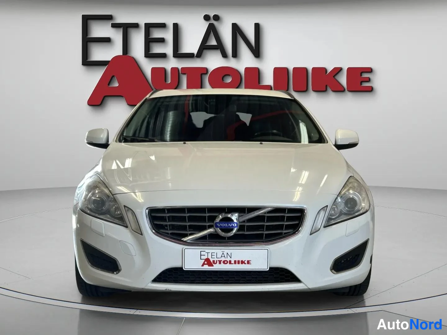 Edestä: Valkoisen farmariauton etupuoli suoraan edestä, etusäleikkö ja Volvo-merkki näkyvissä.