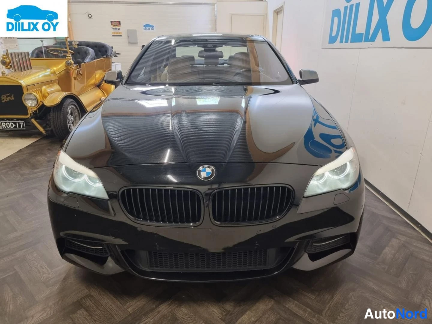 Edestä: Mustan BMW-sedan suora etunäkymä: kaksi munuaisensäleikköä, ajovalot ja etupuskuri näkyvät kohtisuoraan edestä päin.