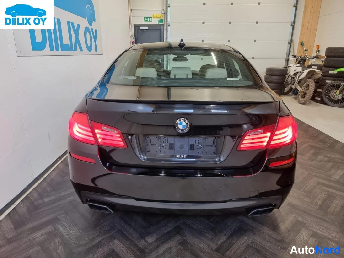 Takaa: Mustan BMW-sedan suora takanäkymä: punaiset takavalot, tavaratilan kannen BMW-merkki ja kaksi pakoputkea näkyvät.