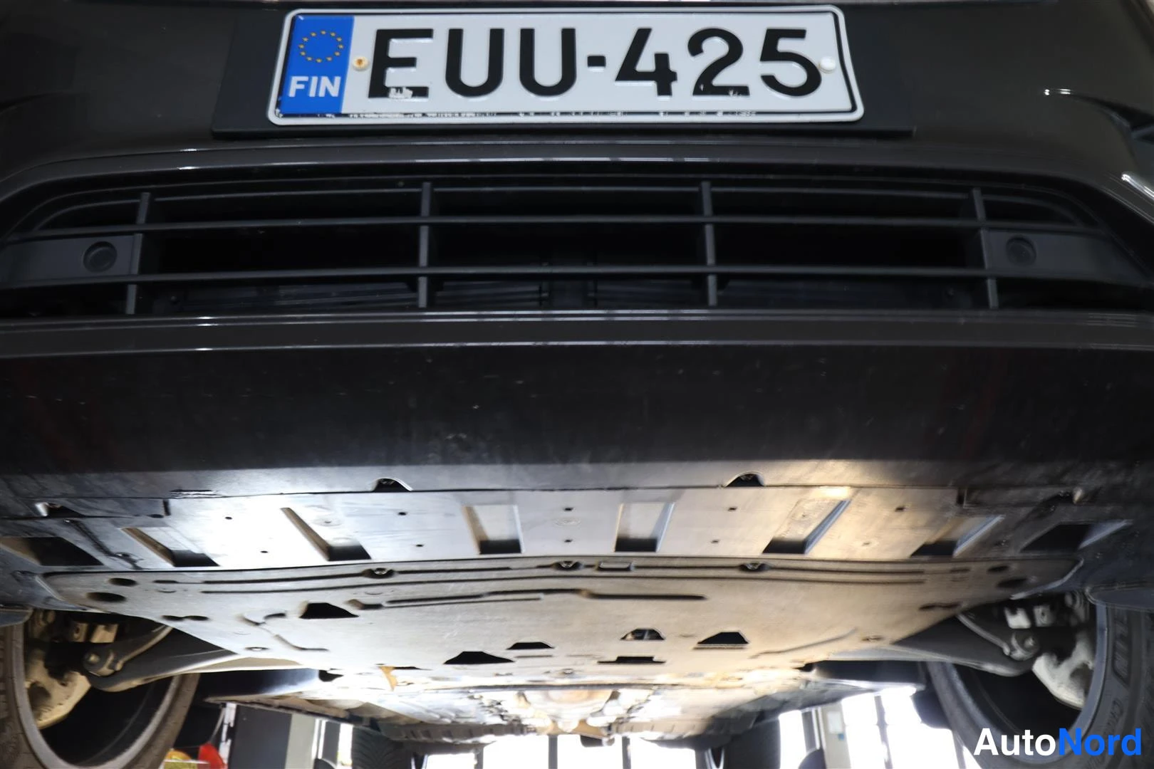 Edestä: Auton etupuskurin alusta ja suoja levitettynä nosturissa, rekisterikilpi.