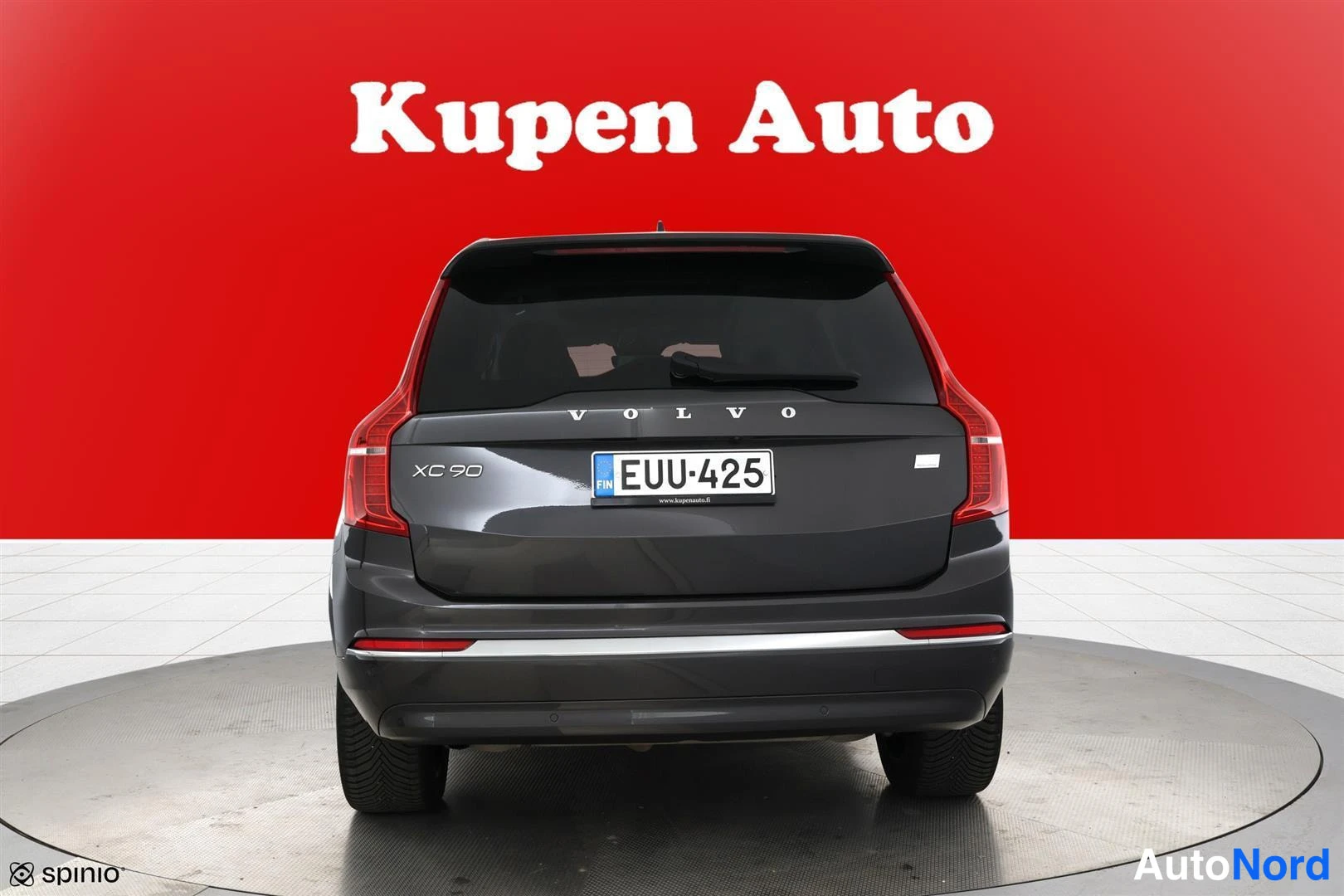 Takaa: Auton takaaotekuva: tummanharmaan tila-auton takaosa, rekisterikilpi ja VOLVO-teksti sivupeitepunaisella taustalla.