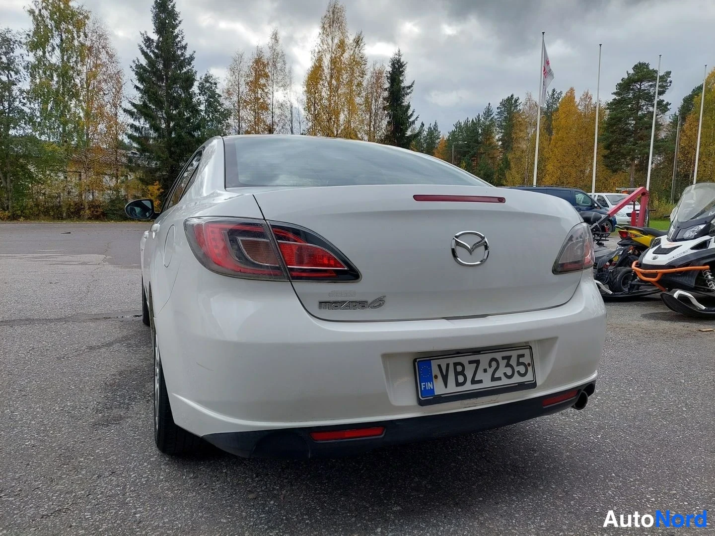 Takaa: Valkoisen Mazda 6 -sedan takapää suoraan takaa; rekisterikilpi, Mazda-merkki ja Mazda 6 -teksti bootissa.
