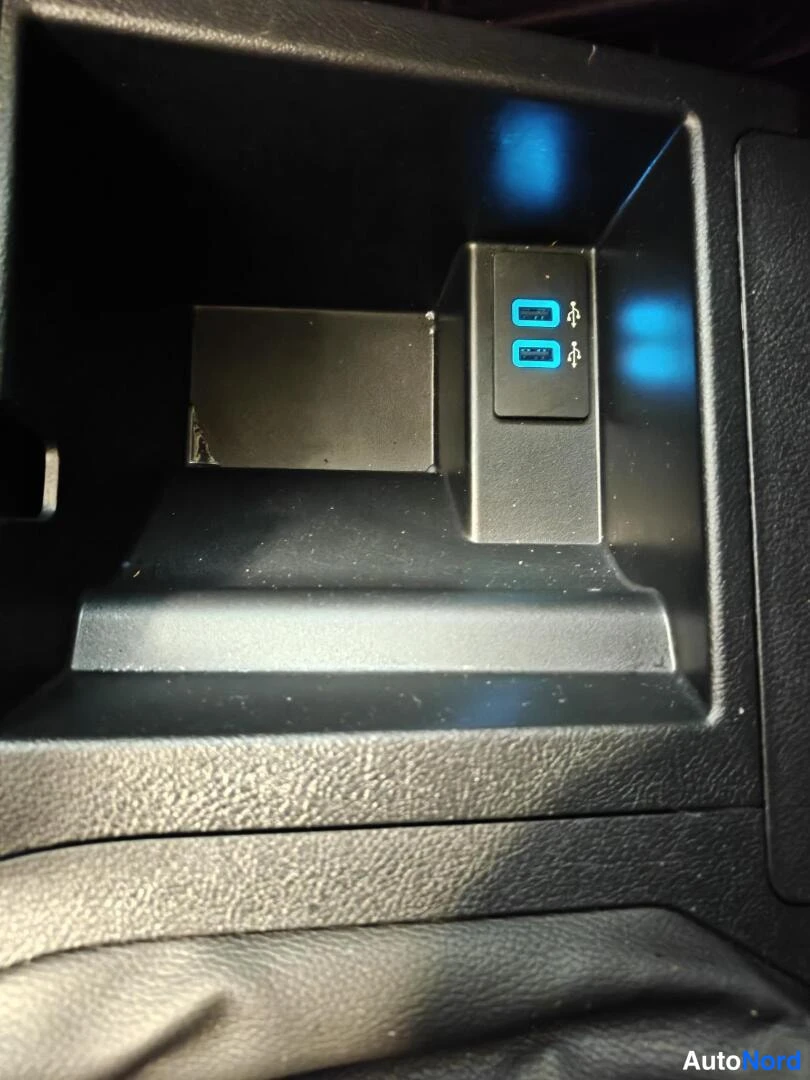 Yksityiskohta: Sisätila: tumma säilytyslokero, jossa kaksi USB-portia sinisellä valaistuksella.