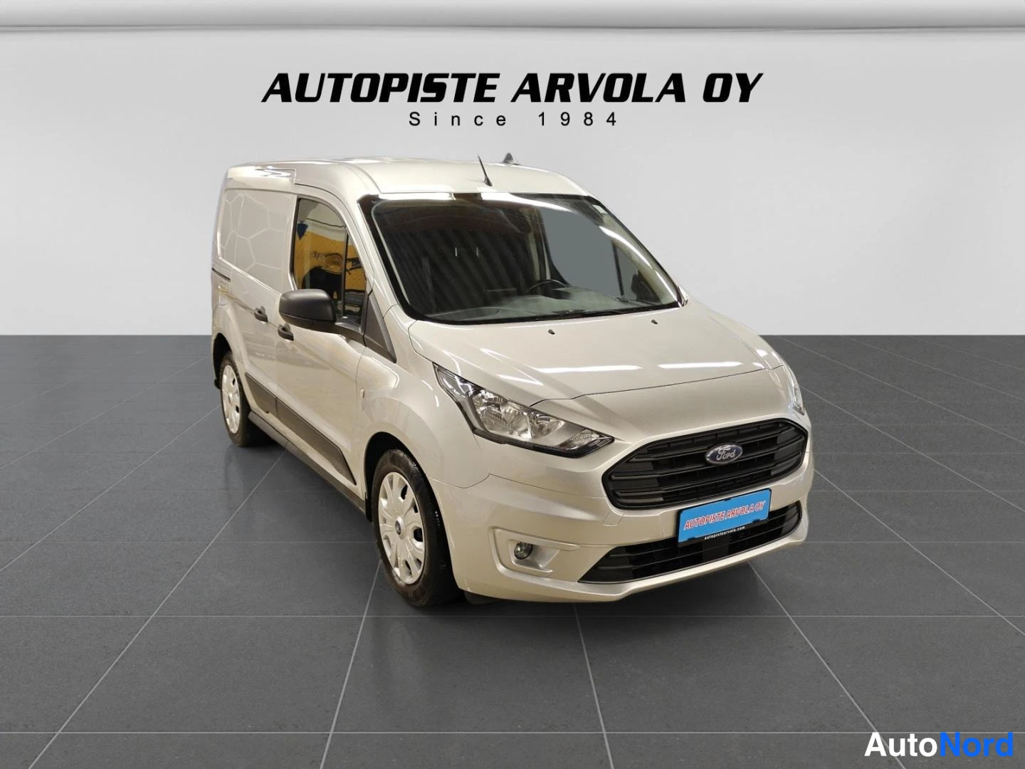 Etuviisto, nokka oikealle: Beige Ford Transit Connect -pakettiauto etukulmasta sisätiloissa, rekisterikilpi Automistelista.com