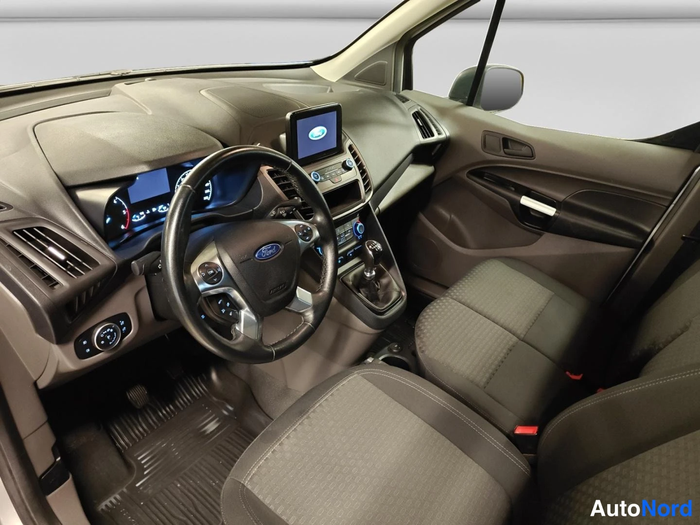 Muu: Ford Transit Connectin ohjaamo vasemmalta: Ford-ohjauspyörä, manuaalivaihtoyksikkö, SYNC-näyttö kojelaudassa ja kaksi tummaa kankaista etuistuinta.