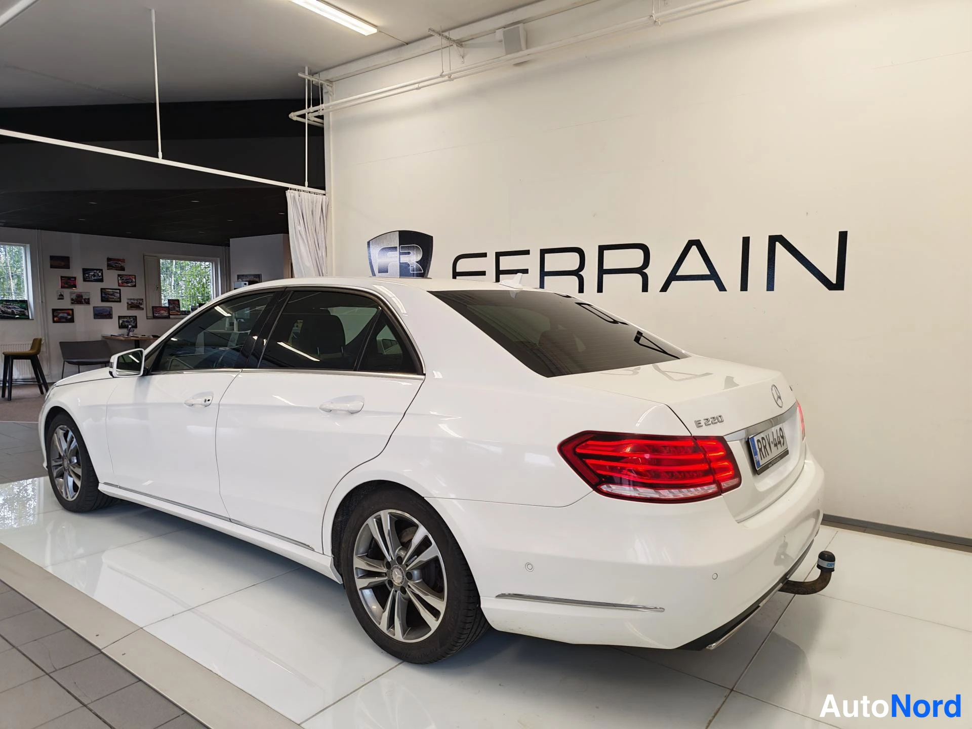 Takaviisto: Valkoisen Mercedes-Benzin takaviisto vasemmalta; takavalot, rekisterikilpi, tavaratilan kannessa E 220 -merkintä ja irrotettava vetoaky näkyvissä.