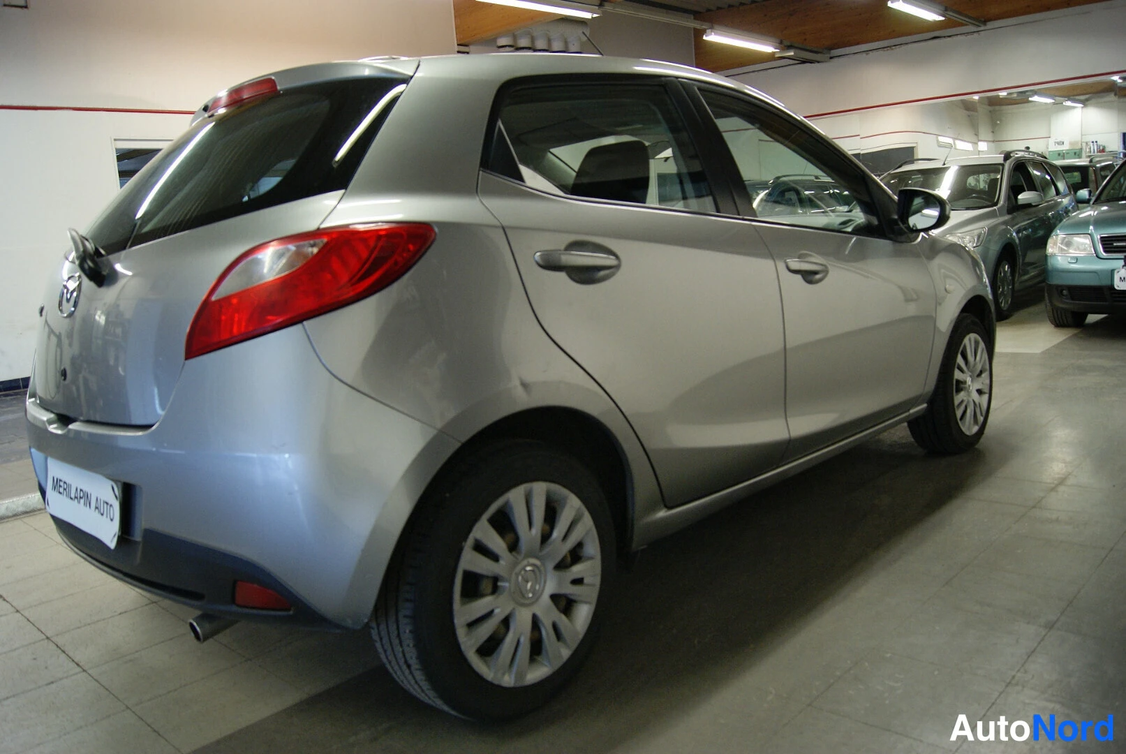 Takaviisto: Hopeanharmaan Mazda 2:n takaosa ja oikea kylki autotilassa.