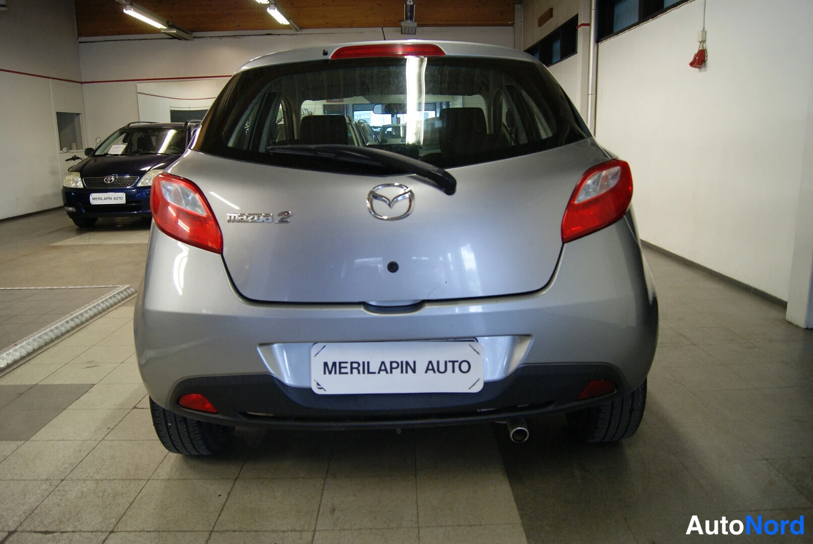 Takaa: Hopeanharmaan Mazda 2:n takaosa: takavalojen ja takaluukun näkymä sisätiloissa.