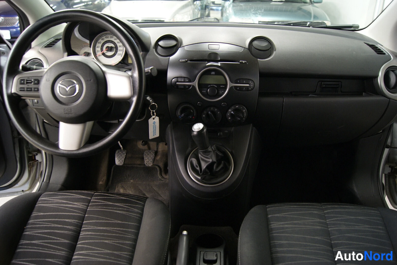 Muu: Ohjaamo vasemmalta: Mazda-ohjauspyörä, analogiset mittarit, manuaalivaihtoein ja keskikonsolin säätimet tummassa kojelaudassa.