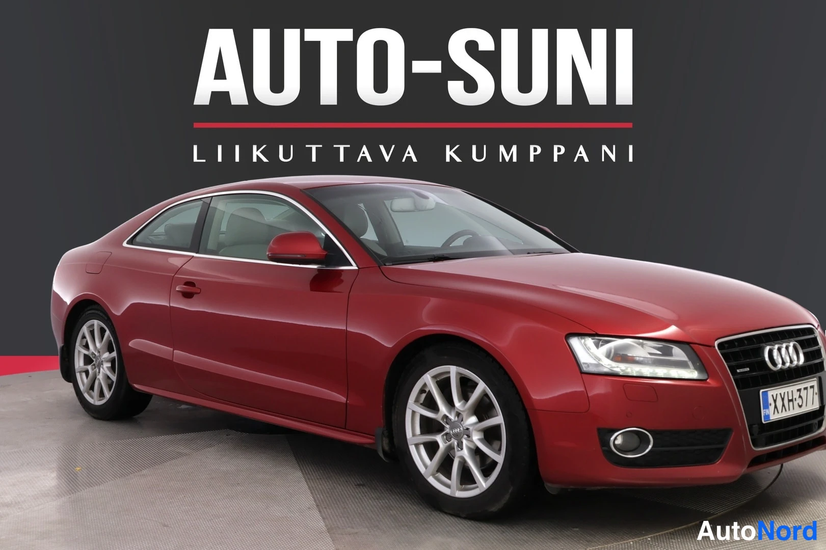 Etuviisto, nokka oikealle: Punainen Audi A5 -coupe etuokolakuvassa studio/environment-taustalla, AUTO-SUNI-logoteksti kuvan yläosassa.