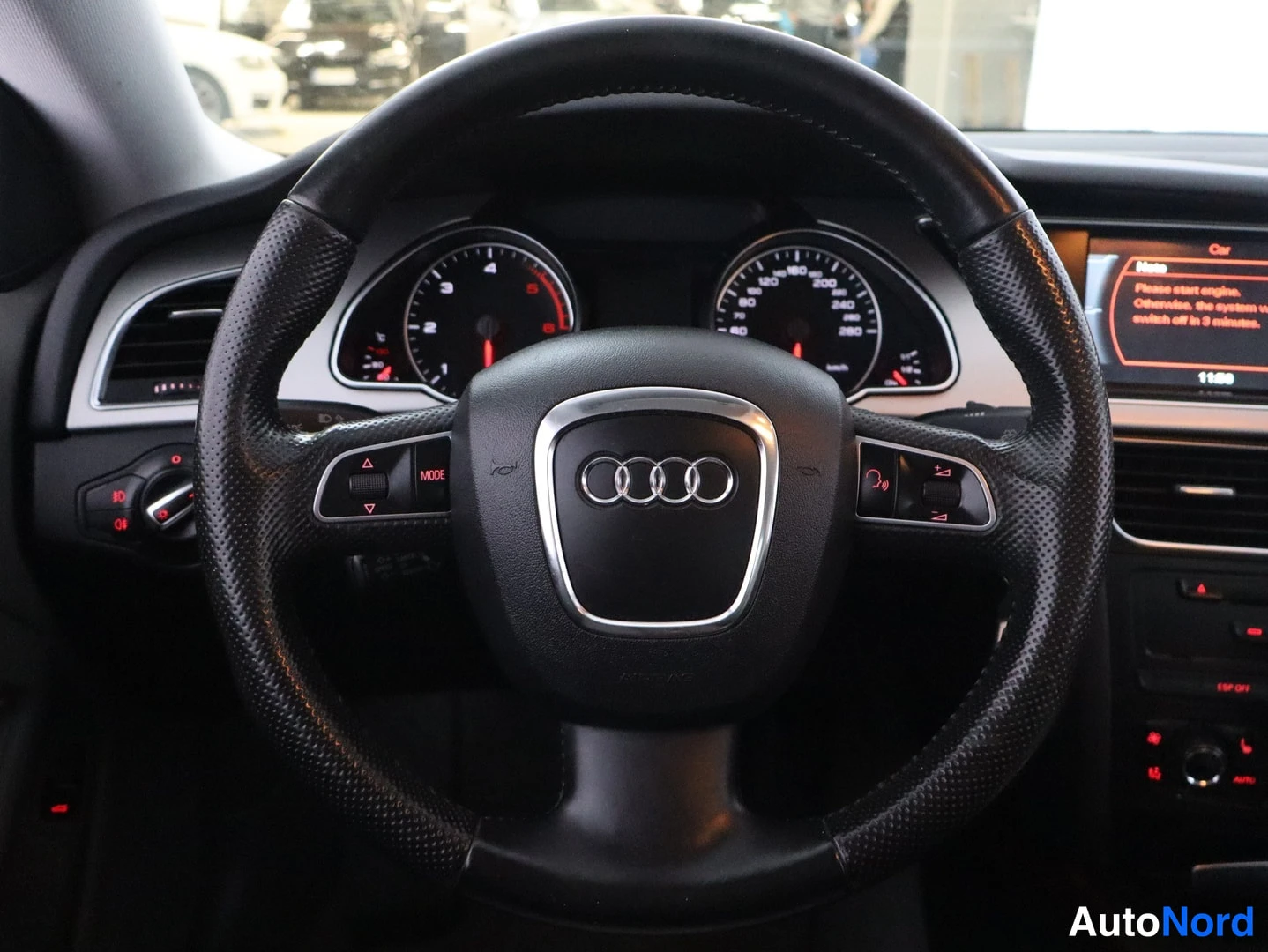 Muu: Ohjauspyörä lähikuvassa keskialueen Audi-renkailla, monitoiminapeilla ja MODE-painikkeella; taustalla mittaristo ja korostusnäyttö, jossa teksti 'Please start e