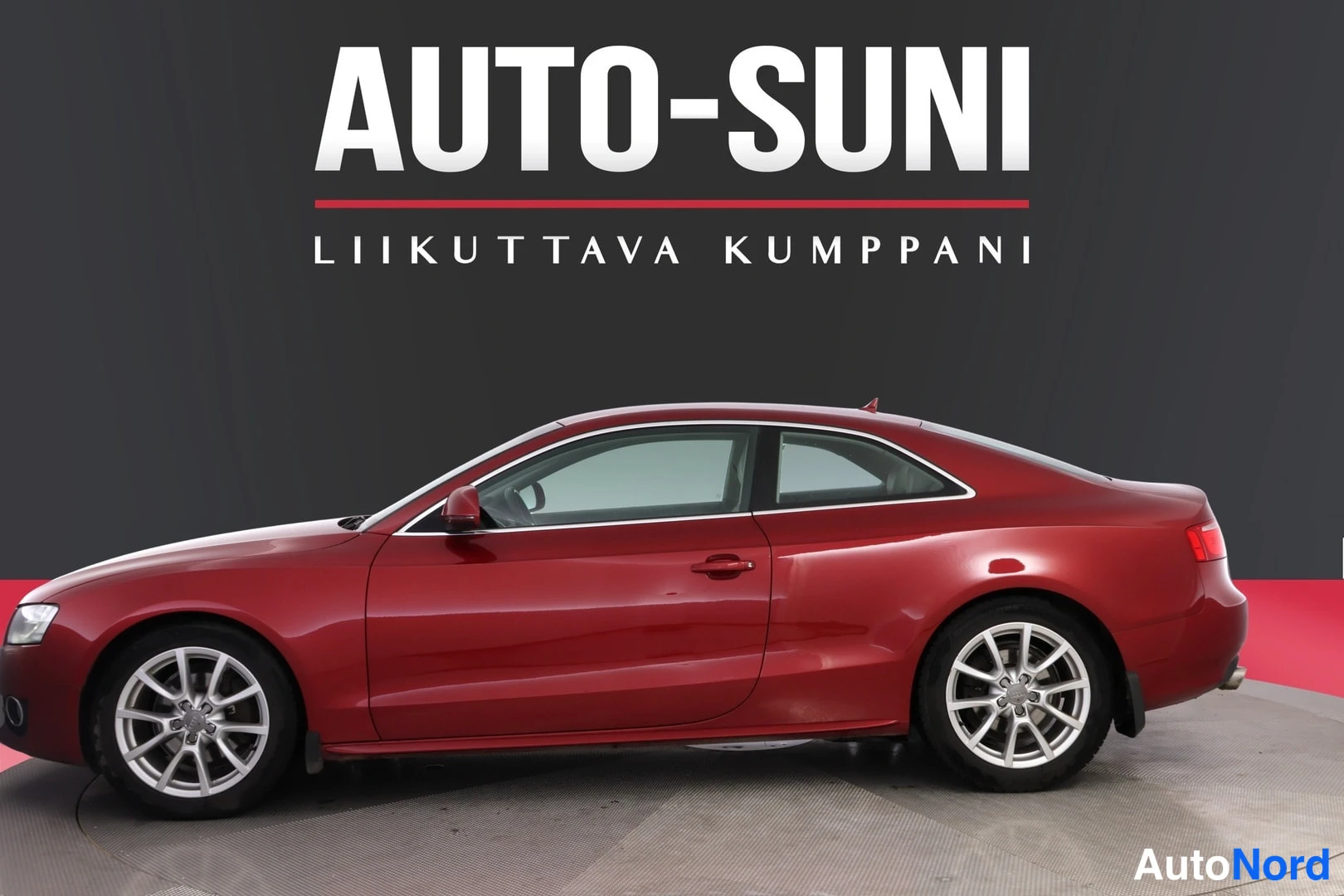 Etuviisto, nokka vasemmalle: Punainen coupé-korinen auto sivulta kuvattuna, kylki ja osa etuosa näkyvissä.
