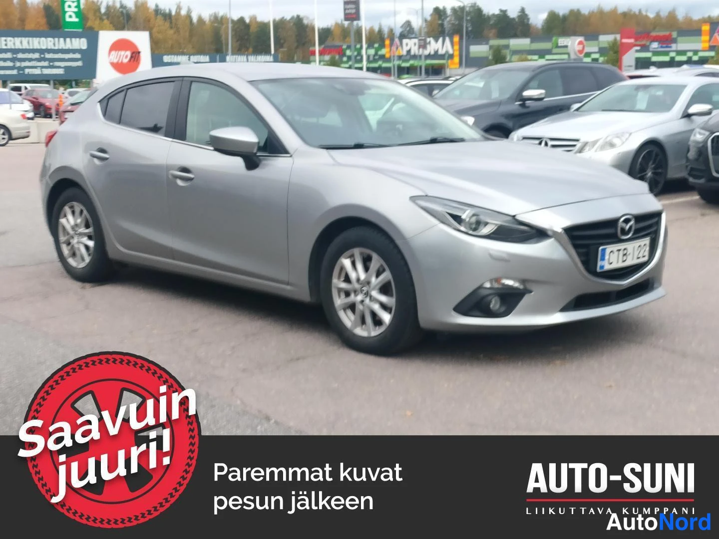 Etuviisto, nokka oikealle: Hopeanvärinen Mazda3 viisiovinen kolmannesvuoronurkassa pysäköintialueella, rekisterikilpi.