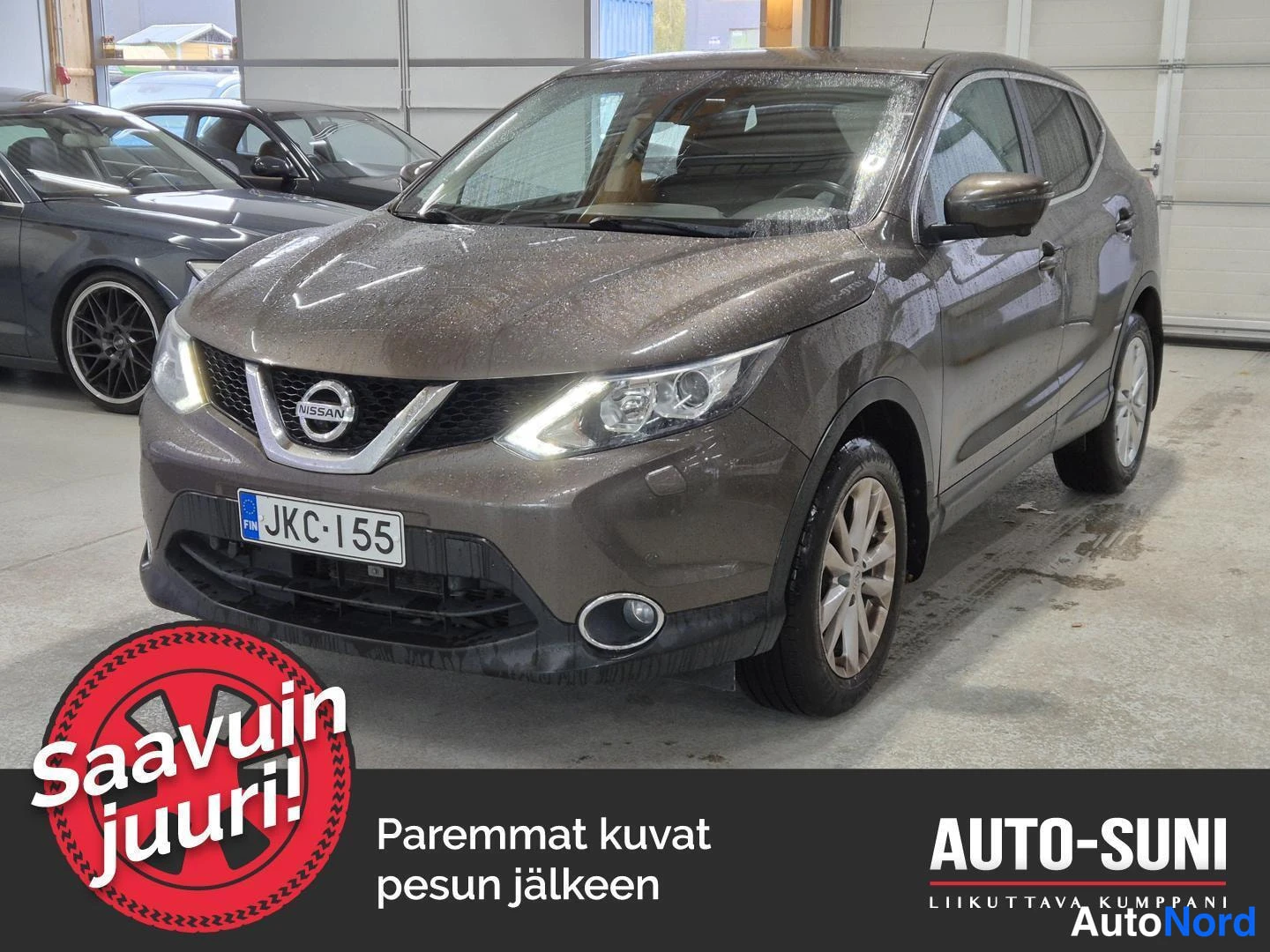 Edestä: Ruskeanharmaan Nissan Qashqain etukolmannelakikuva sisätiloissa, rekisterikilpi, keula vasemmalla.