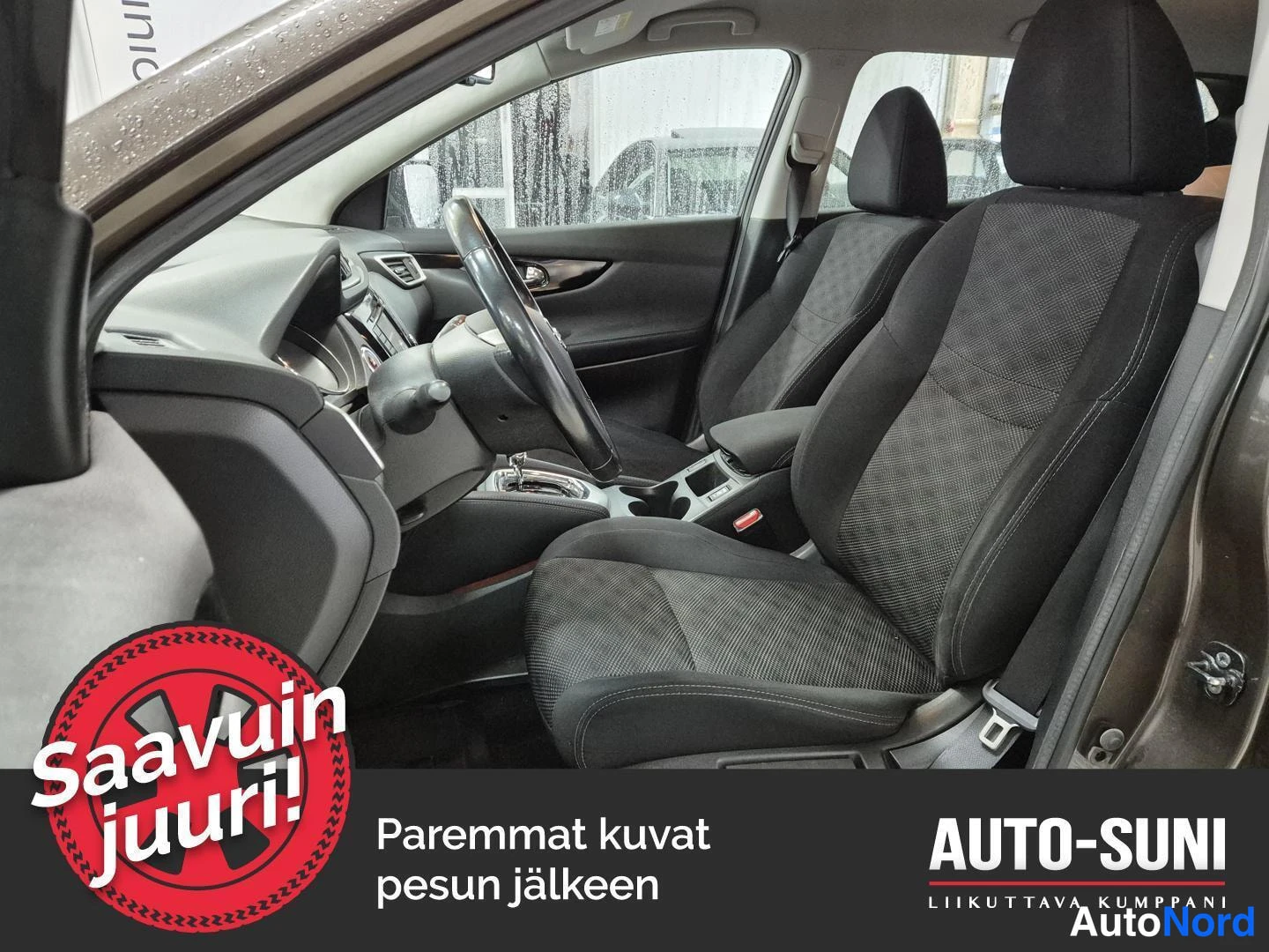 Etuviisto, nokka vasemmalle: Nissan Qashqain etumatkustamo ohjauspyörineen ja tummine tekstiilipenkkeineen, kuvattu avoimesta ovesta.