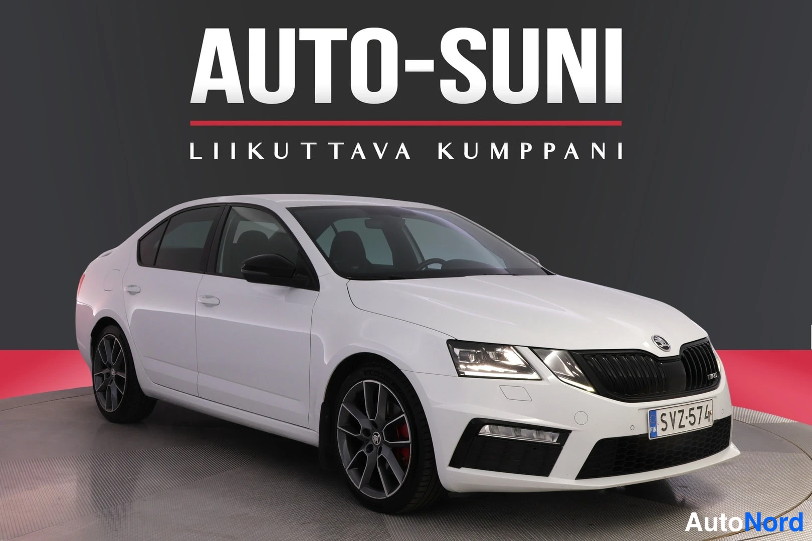 Etuviisto, nokka oikealle: Valkoinen Škoda Octavia -sedan kolmeneljännesetunäkymä oikealta, tummaa vanteita levyillä etupyörät, rekisterikilpi, studio-tausta.