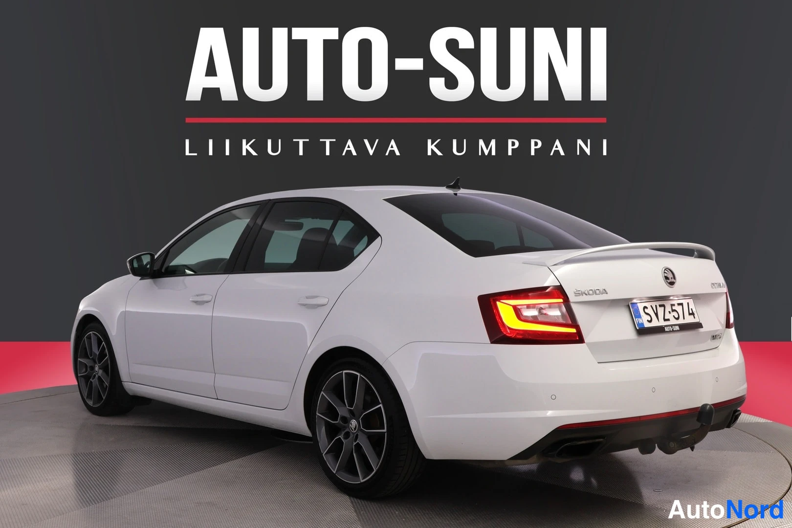 Takaviisto: Valkoinen Škoda Octavian takaosa vasemmalta kolmeneljännekseltä, rekisterikilpi, SKODA-merkintä takaluukussa, kattospoilerin näkyessä.