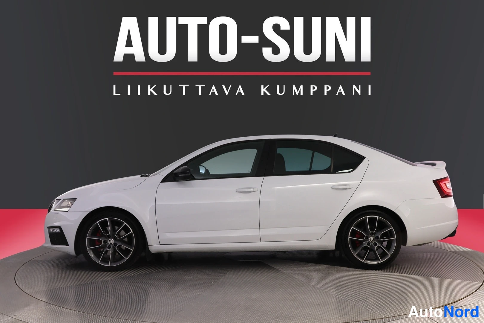 Etuviisto, nokka vasemmalle: Auton etukulma vasemmalta: valkoinen neliovinen sedan, mustat kevytmetallivanteet, punaiset jarrusatulat.