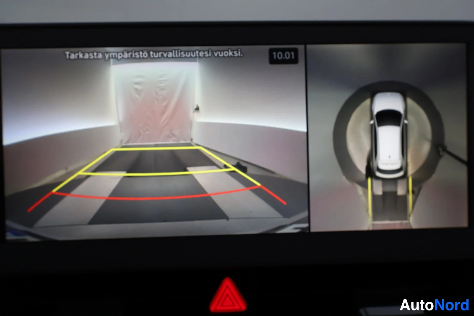 Muu: Infotainment-näyttö näyttää takakameraa ja 360-asteisen ympärystönäkymän; teksti 'Tarkasta ympäristö turvallisuutesi vuoksi' ja kello 10.01.