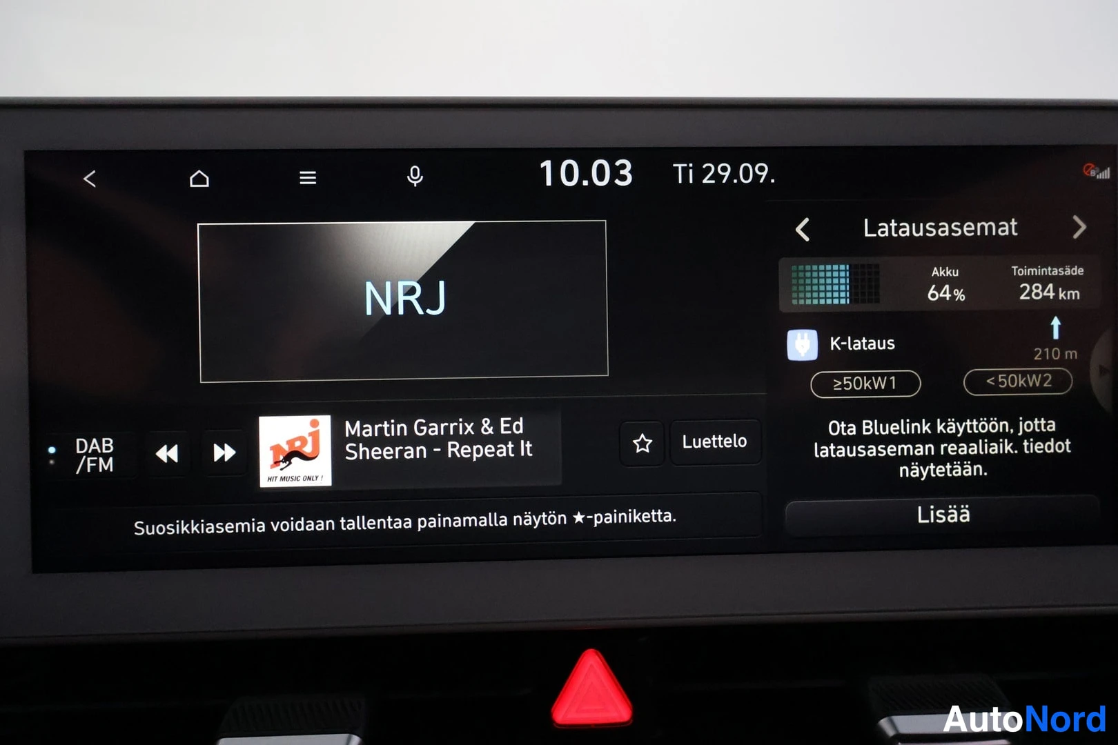 Muu: Auton multimedianäyttö näkyy NRJ-radioasemalla Martin Garrix &amp; Ed Sheeran kappaleella Repeat It, latausasemat-näkymässä akun varaustaso 64 % ja toimintamatk