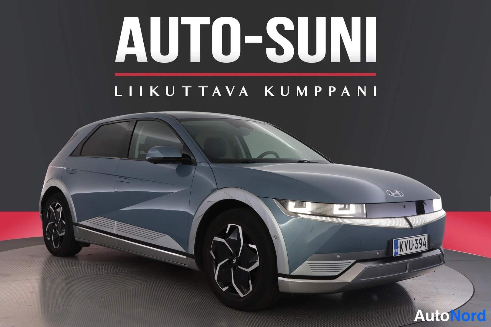 Etuviisto, nokka oikealle: Sinertävänharmaa Hyundai IONIQ 5 -sähköauto etu- ja sivusivulta studiovaalealla taustalla, rekisterikilpi.